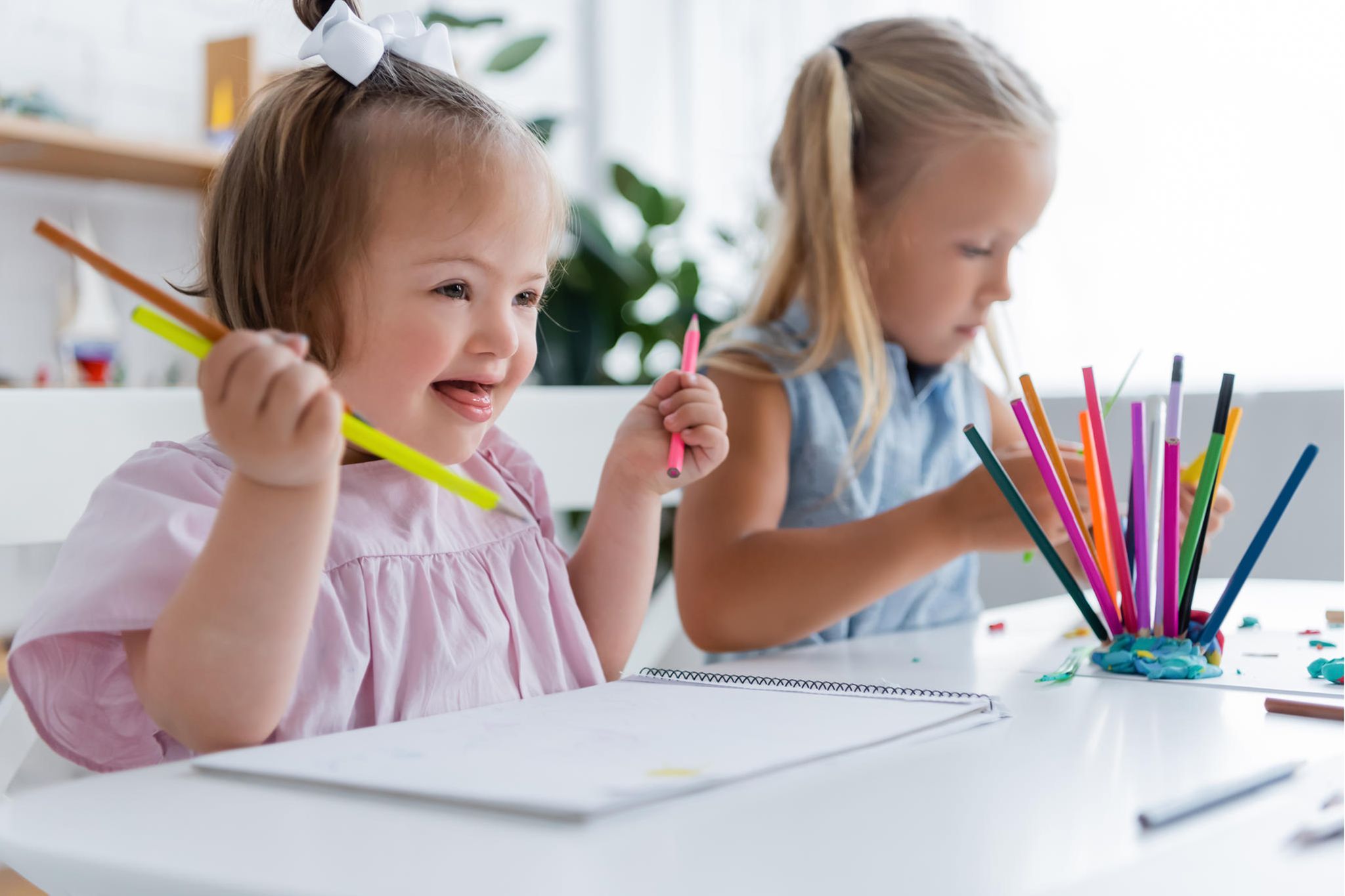 Bild wie 2 Kinder an einem Tisch sitzen und malen