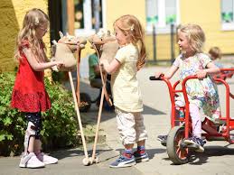 Ein Bild von 2 Kindern mit Steckenpferd. Rechts daneben steht ein weiteres Kind mit einem Dreirad